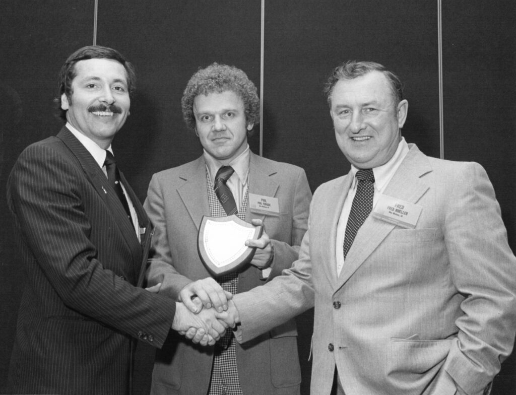 Three men shaking hands, award presentation.